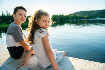 Fototapeta na wymiar Cute childs brother and sister sitting on a wooden platform by the lake.