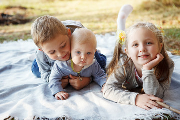 Three children, elder brother, sister blonde and 7-month-old boy with blue eyes are lying on a rug in the autumn forest.