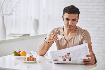 Young man enjoying breakfast and reading newspaper