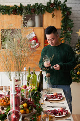 Handsome young Vietnamese man with wine glass standing at Christmas table