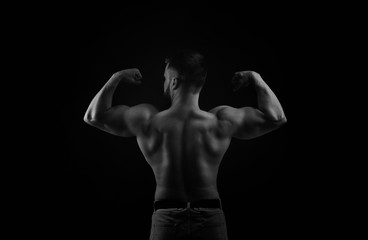 Bodybuilder black and white portrait. Muscular man stands back and shows biceps.