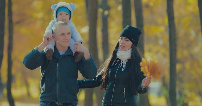 Happy father carrying his smiling son next to mother in the autumn park. Happy family together
