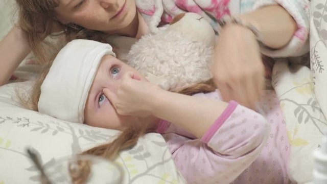 Sick girl with fever. Child with fever: a woman caring for a child and medicating