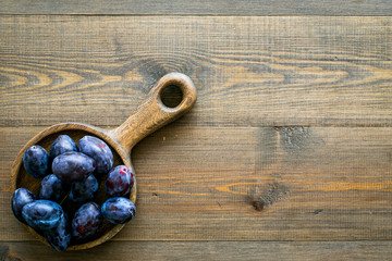 Plums on dinning table. Fresh raw purple plum in wooden bowl on wooden background top view copy space