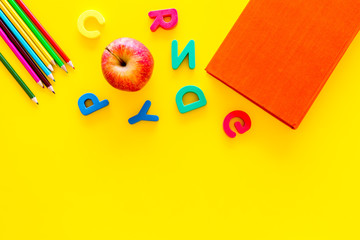 Primary school concept. Letters of english alphabet, apple and color pencils on yellow background...