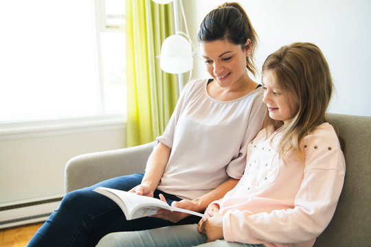 Mom with little girl reading book in sofa