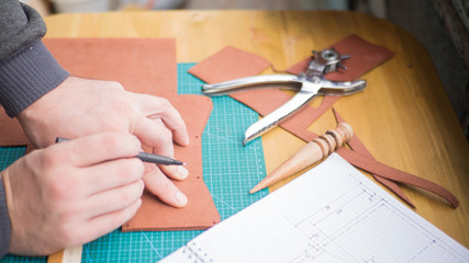 Tanners hands at work with leather. Revolver punch and a slicker. Selected focus, close up.
