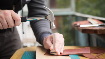 Tanners hands at work with step punch, hammer and leather. Selected focus, close up.