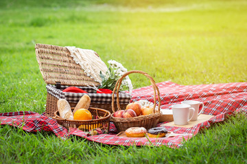 Picnic basket with fruit and bakery on red cloth in garden.