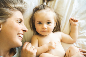 Mother and his baby daughter on bed having fun