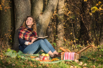 Young beautiful girl in the park at a picnic reading a book and smiling