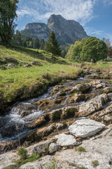 Wonderful creek running through enchanted scenery in the Swiss alps with Fly fisherman in background and farm and massive mountain makes a peaceful scenery in the alps