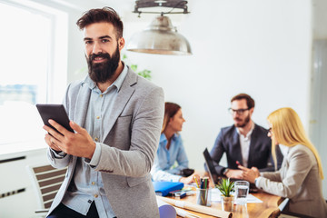 Portrait of young businessman using digital tablet while colleague in background