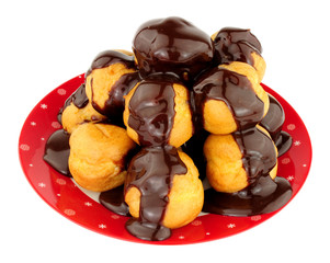Plate of cream filled profiteroles with chocolate ganache sauce poured over isolated on a white background