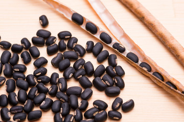 木のテーブルの上の黒小豆のさやと沢山の豆