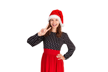 confident happy and outgoing woman in dress, showing victory or peace gesture and winking with broad smile at camera. emotional girl in santa claus christmas hat isolated on white background