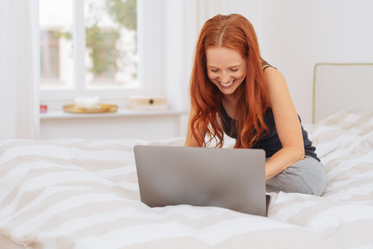 Young woman sitting on a bed surfing the internet