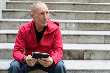 Bald senior man thinking and looking at distance while holding d