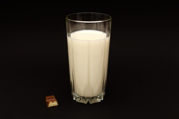 Glass of milk and a piece of chocolate on the black background
