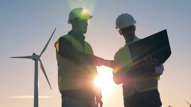 Renewable electririty, green energy concept. People working together near windmills.