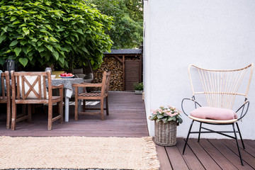 Pink flowers next to armchair on wooden terrace with chairs at table next to tree