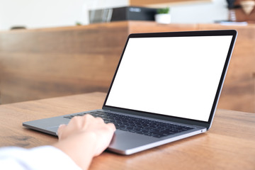 Mockup image of hand using and typing at laptop with blank white desktop screen on wooden table in office