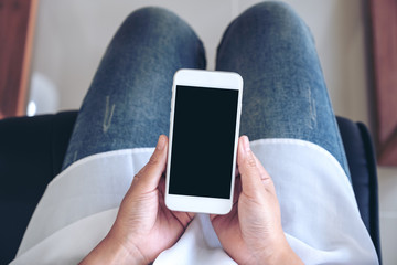 Top view mockup image of woman's hands holding white mobile phone with blank black screen