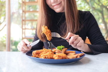 Closeup image of a beautiful asian woman using knife and fork to eat fried chicken and french fries in restaurant