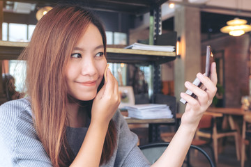 Closeup image of an asian woman looking in a mirror while putting on makeup