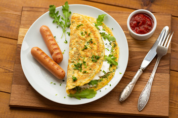 Omelette with herbs, soft cheese, grilled sausages and tomato sauce. Delicious breakfast
