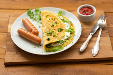Omelette with herbs, soft cheese, grilled sausages and tomato sauce. Delicious breakfast