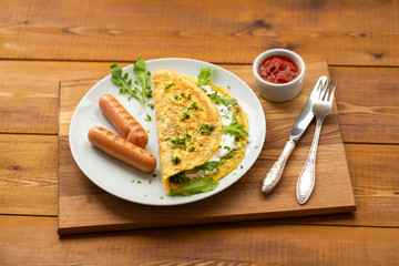 Omelette with herbs, soft cheese, grilled sausages and tomato sauce. Delicious breakfast