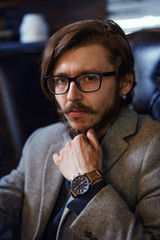 A bearded man with a clock on his hand is sitting in a chair. Male portrait