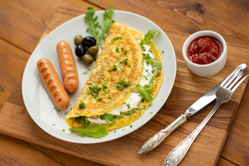 Omelette with herbs, soft cheese, grilled sausages, olives and spicy tomato sauce. Delicious breakfast