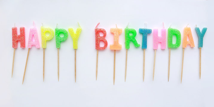 Multi-coloured Happy Birthday candles on white background.