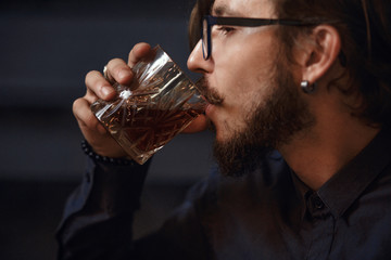 The guy takes a sip of whiskey. Close-up of the face on the left side.