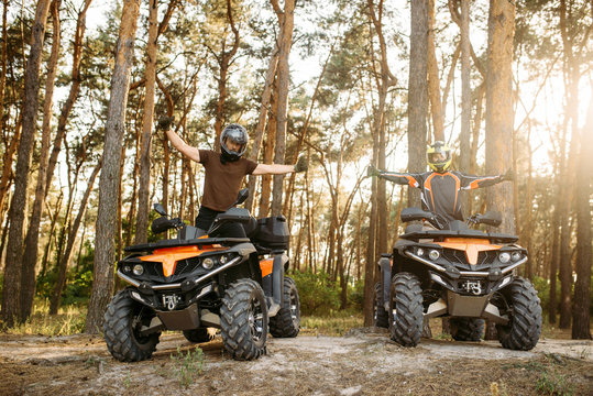 Two atv riders in helmets raise their hands up