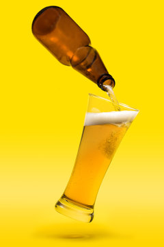 Floating glass and beer bottle on yellow background