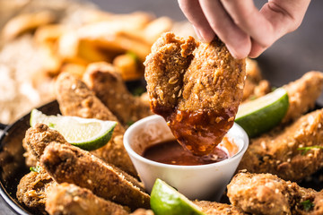 Hand holding fried chicken wing with chili sauce.