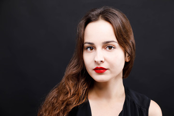 Portrait of pretty serious brunette woman wearing black dress standing on the black background