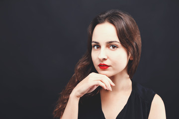 Portrait of pretty serious brunette woman wearing black dress standing on the black background, black friday concept