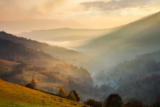 amazing glowing sunrise in mountains. countryside in fall colors. village down in the valley in haze and fog