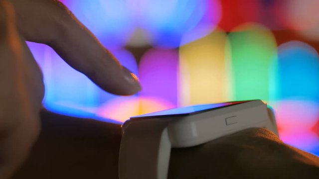 Young woman using wearable smartwatch computer device in the city - scrolling and touching. Evening time, twilight, colourful bokeh background. Relax, entertainment and technology concept