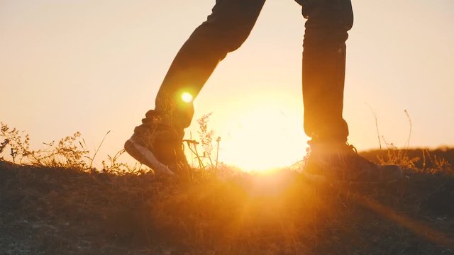 Hiker walking outdoors at sunset on the rock. Legs in trekking boots go along the mountain ridge against the backdrop of the sun Close up of leg walking in slow motion. Travel and adventure concept.