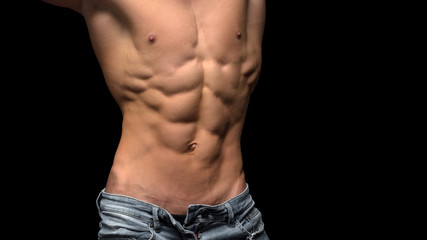 Torso of strong man in jeans against dark background.