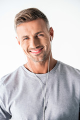 Obraz premium smiling adult man in blank grey t-shirt and earphones looking at camera isolated on white
