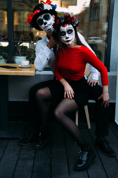 A couple, wearing skull make-up for. All souls day. Boy and girl sugar skull makeup.painted for halloween sit in a cafe. dead in the city. zombie walk.