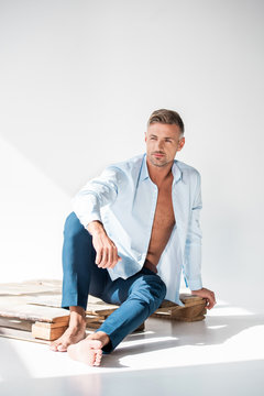 handsome sexy man sitting on wooden pallet on white and looking away