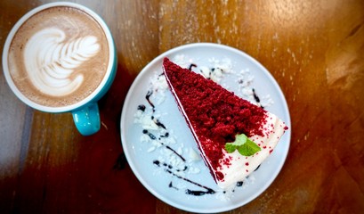 close up of A cup of hot latte art or cappuccino coffee and red velvet cake on wooden table 