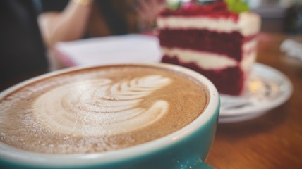 close up of A cup of hot latte art or cappuccino coffee and red velvet cake on wooden table 